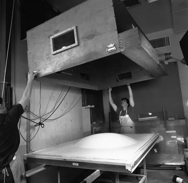 Two men bring down the top hand of the press onto the paper pulp sheet