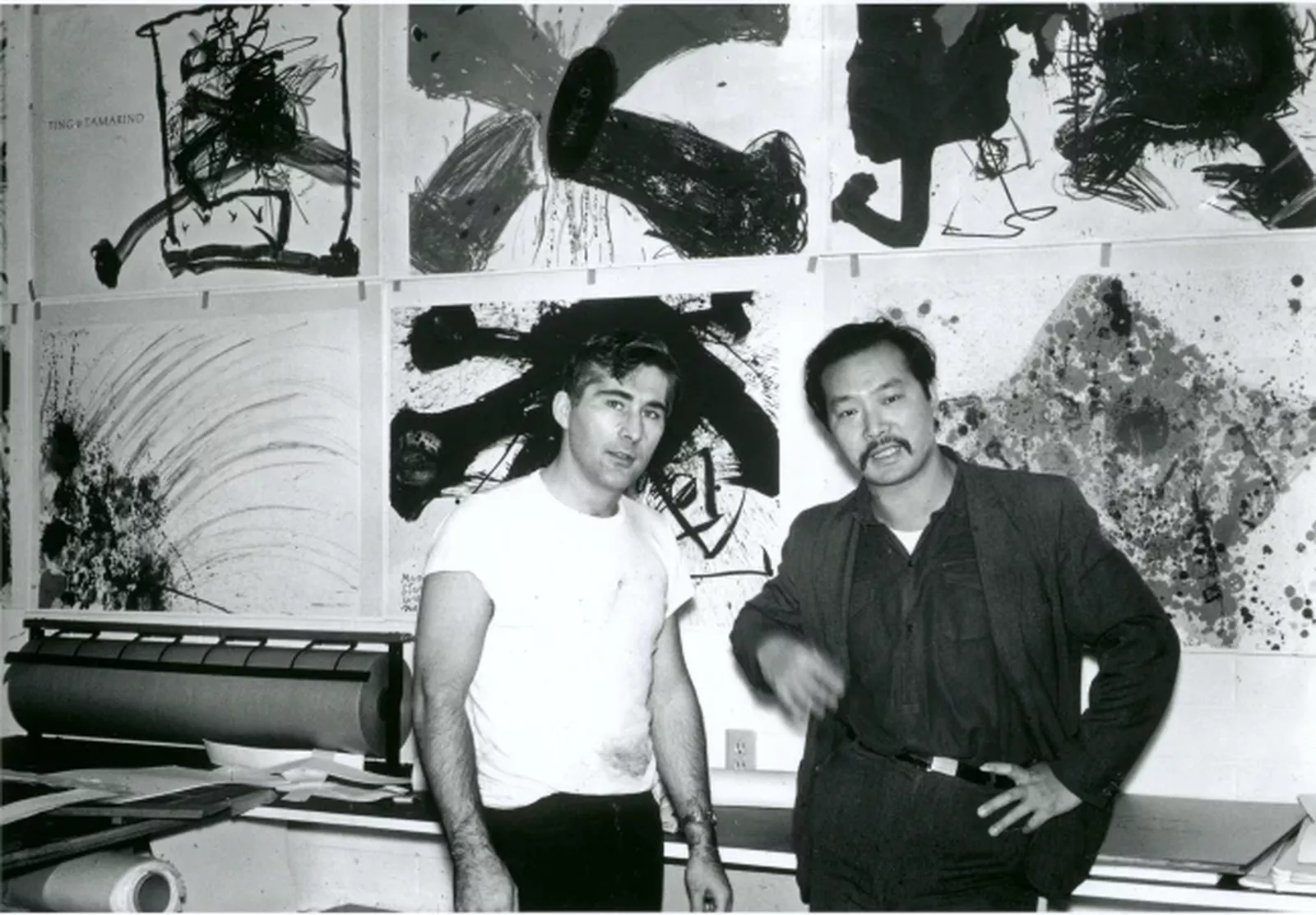 Black and white photograph of Tamarind’s Technical Director Kenneth Tyler, with Artist-fellow Walasse Ting, in front of Ting’s lithographic suite,
