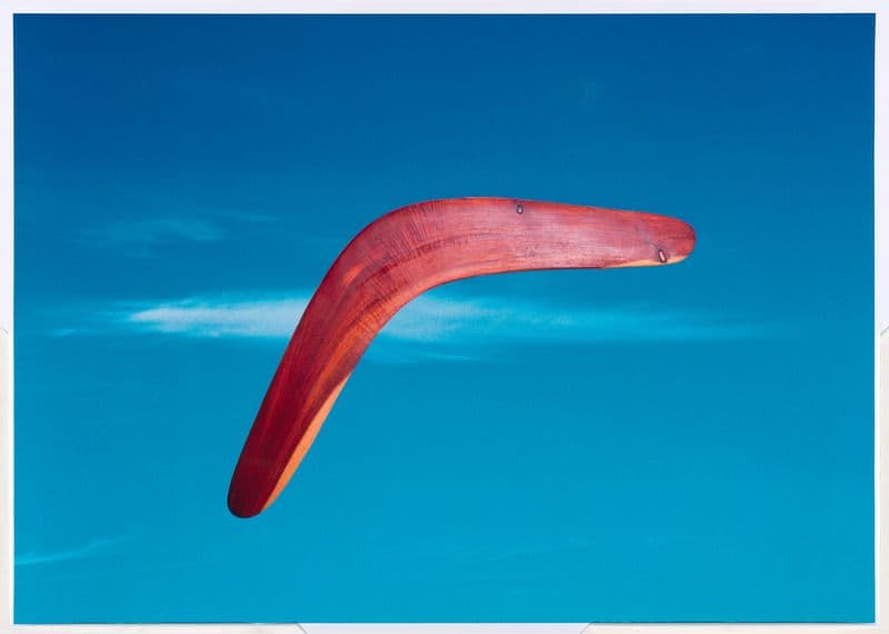 A red timbre boomerang is flying through a bright blue sky