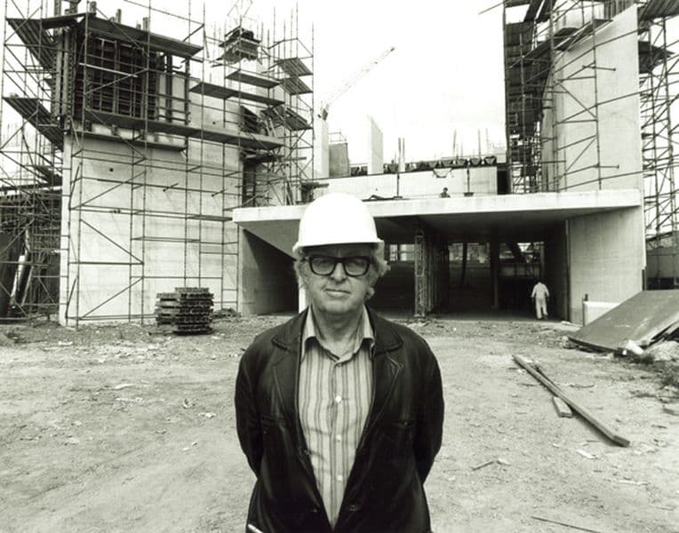 Black and white portrait of a mean wearing a hard hat in front of a building under construction