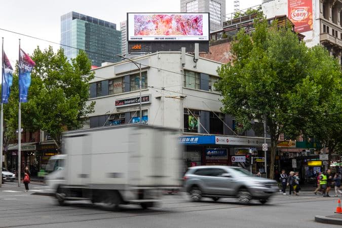 Image of indigenous artwork on billboard on top of building on a busy city street