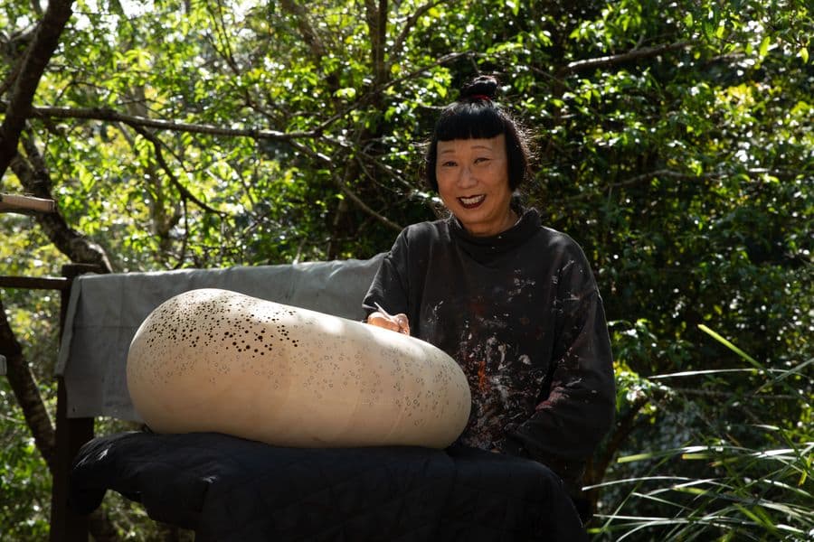 Artist Lindy Lee sitting outdoors with a maquette of her sculpture Ouroboros