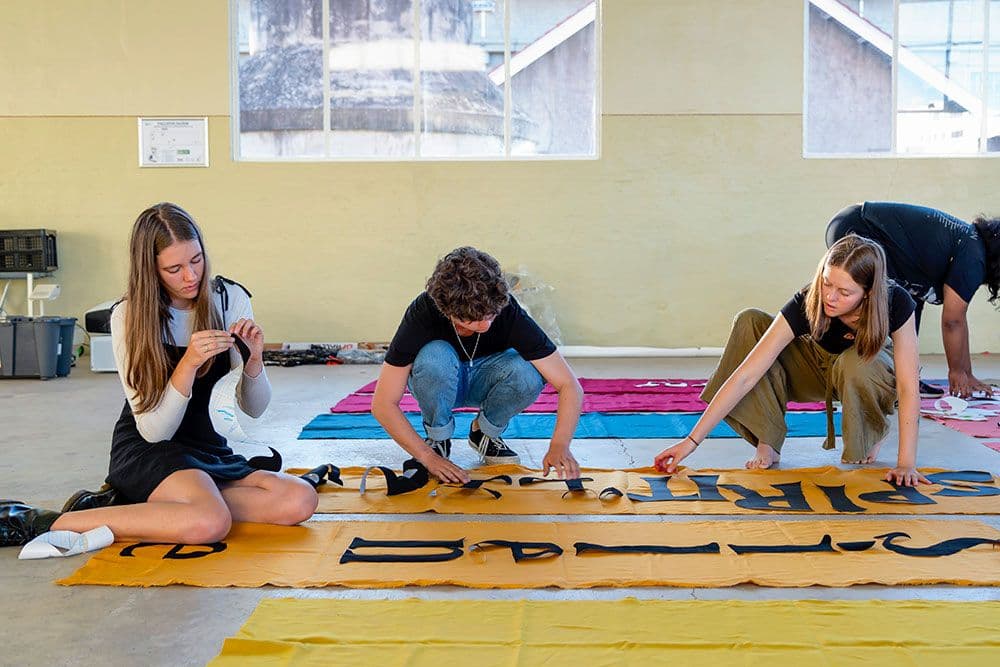 Four people sitting on the floor working on a piece of orange fabric