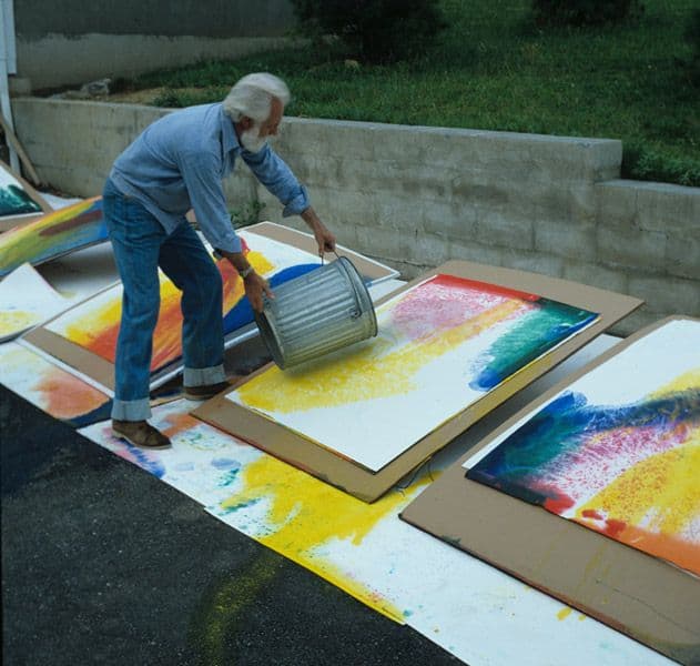 Paul Jenkins using a bucket to throw paint onto a canvas in a parking lot