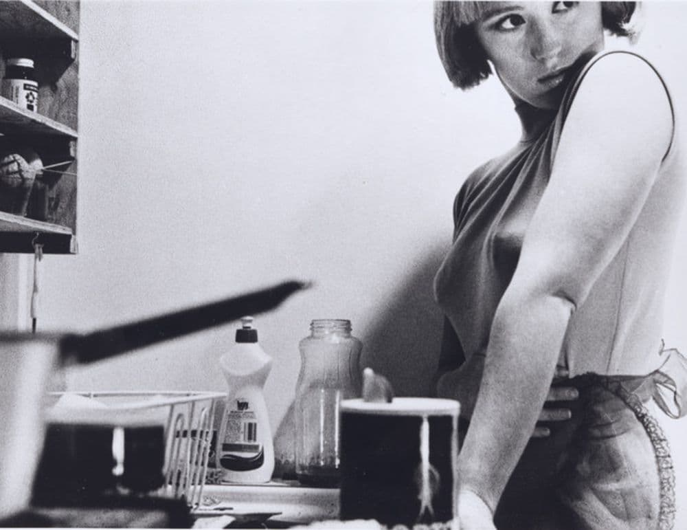 Black and white photograph of a woman standing by a kitchen sink