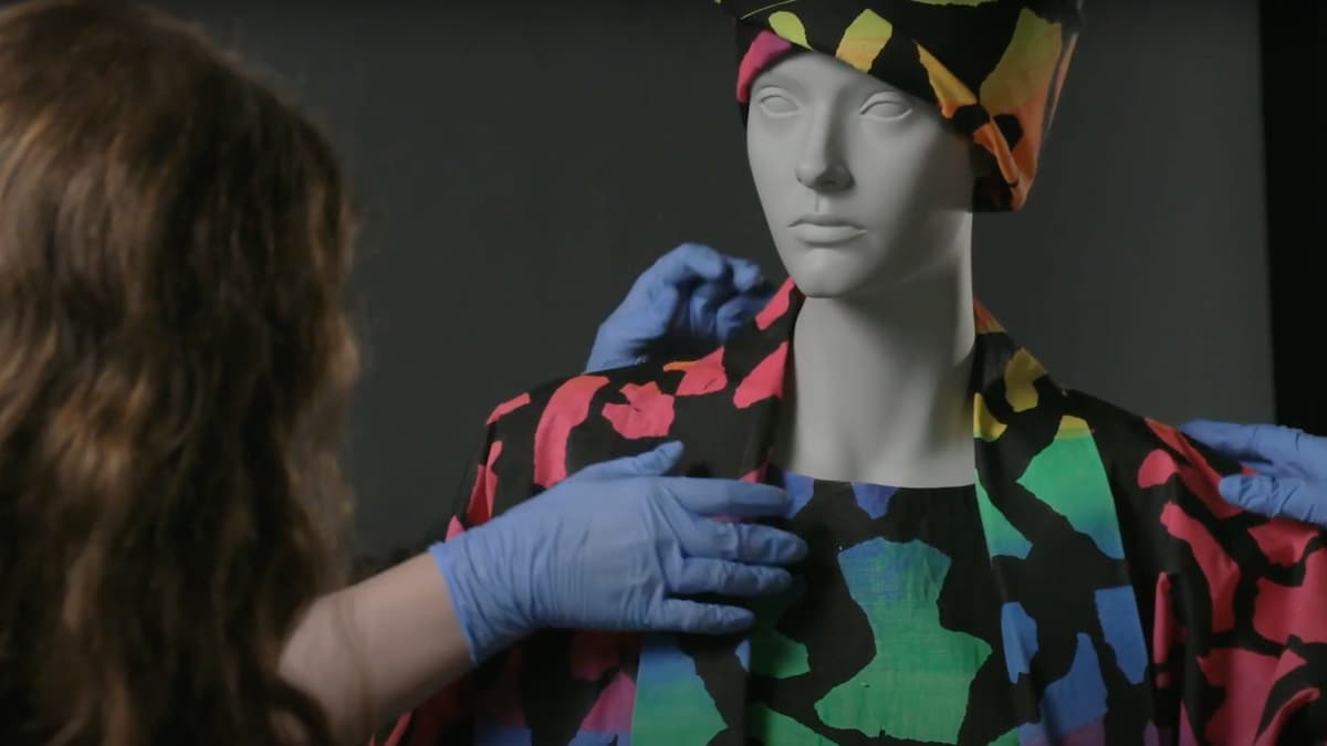 A video still of a woman examining clothes on a mannequin