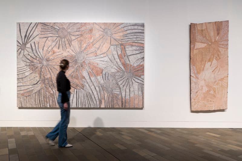 Woman in dark clothing walking in front of art in gallery space