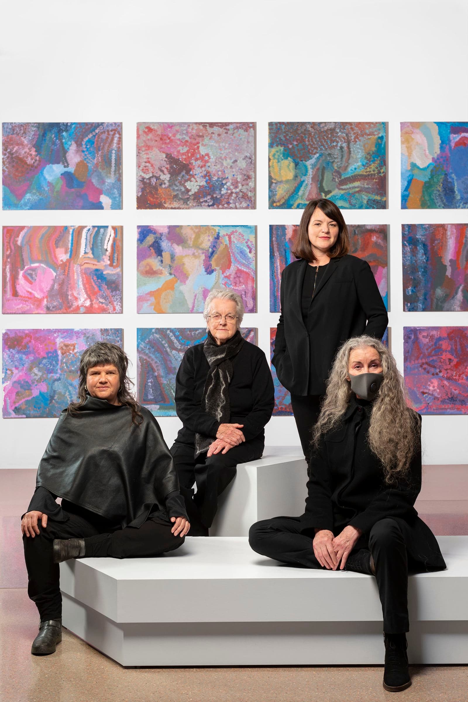 Four women sit against a series of colourful paintings.