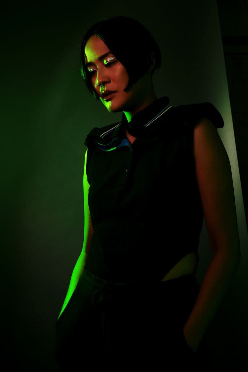 A woman stands lit to the side with green