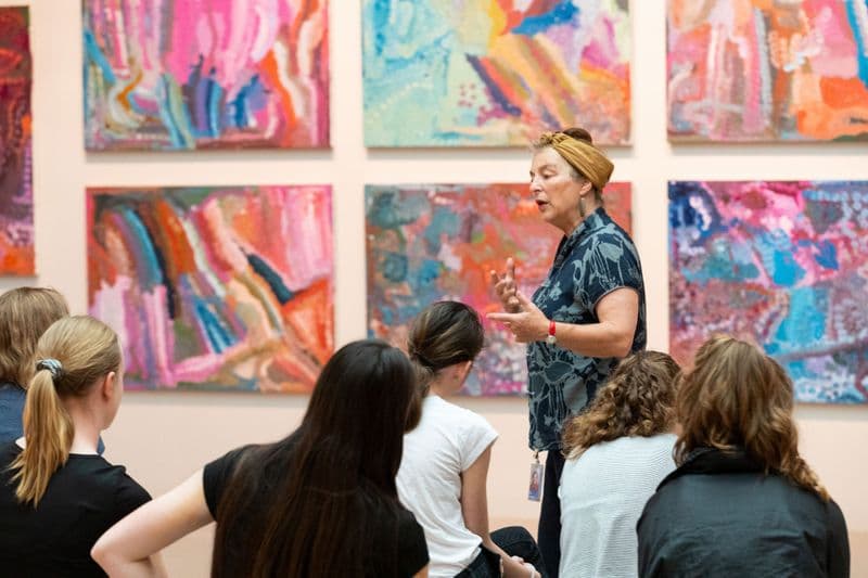 Photograph of speaker gesturing at colourful artwork in front of group