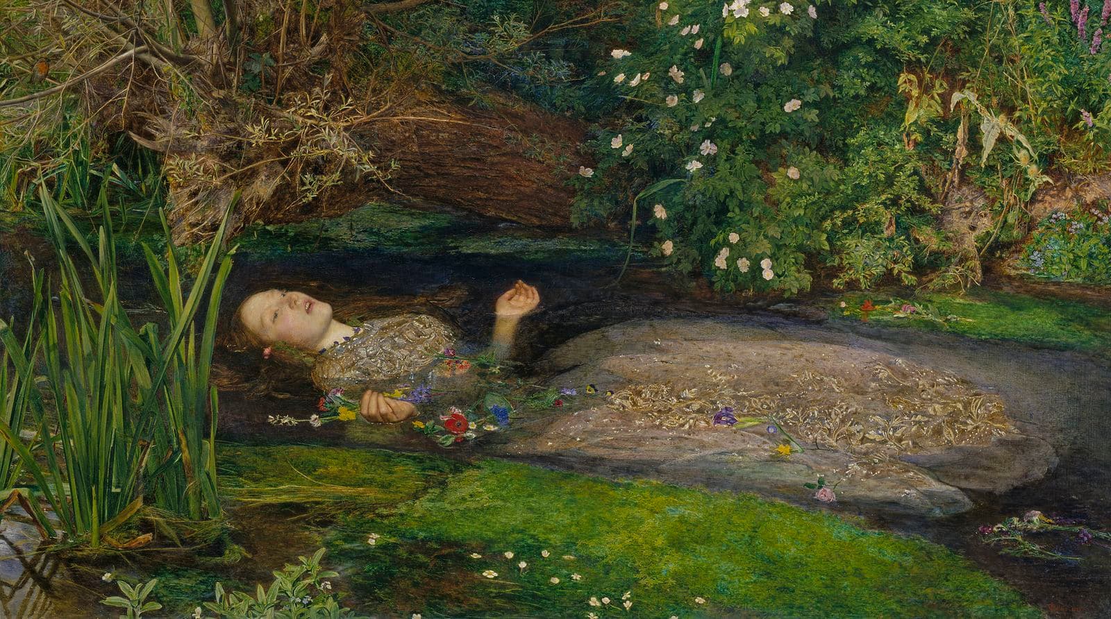 a young woman in a bejewelled dress floats face up in a stream surrounded by greenery and flowers