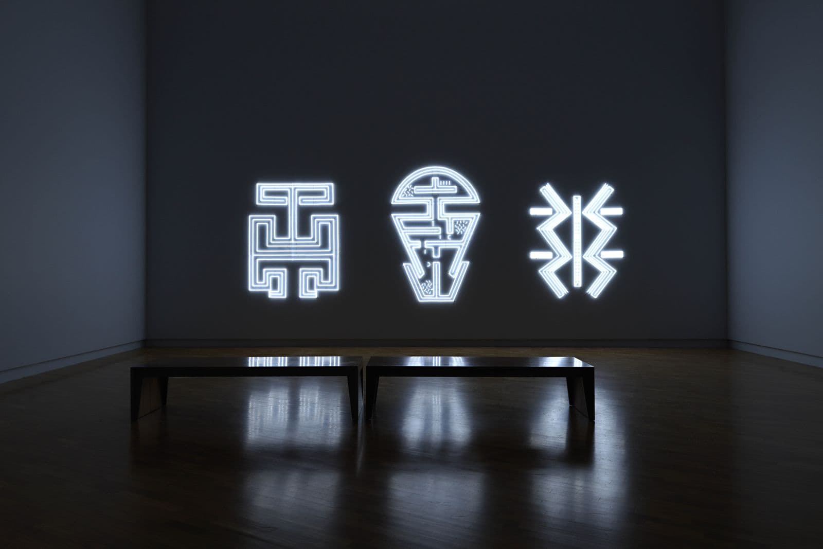 Three large linework neon light designs are hung across a wide wall