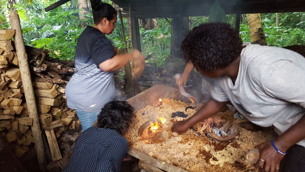 Photograph of three women building a traditional fire out of coconut husks