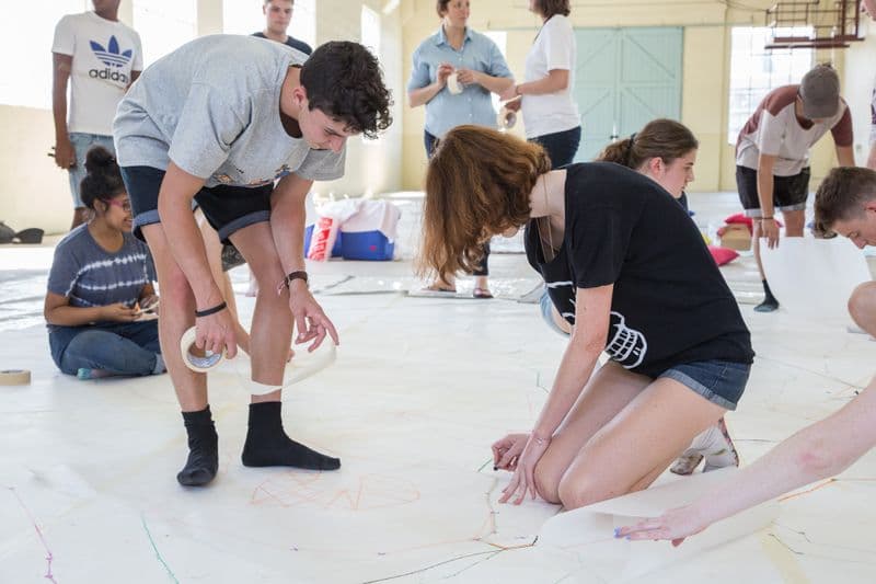 a group of young people are working together to create art on large pieces of paper laid down on the floor