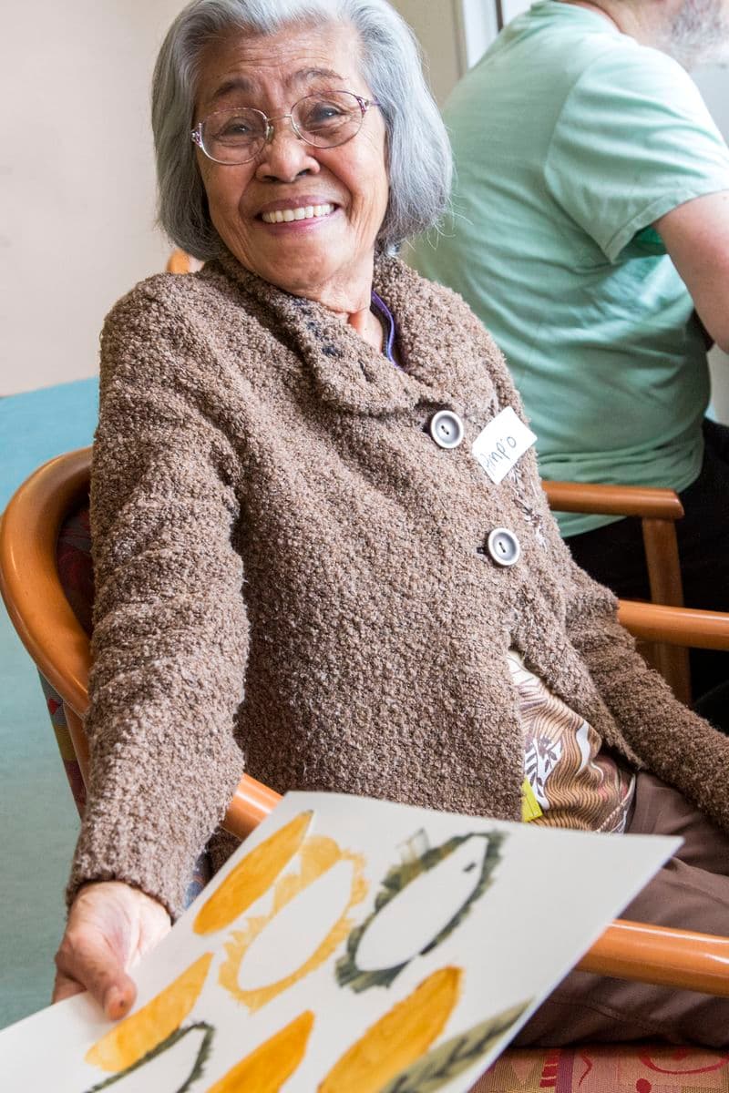 Photograph of woman seated showing artmaking to camera