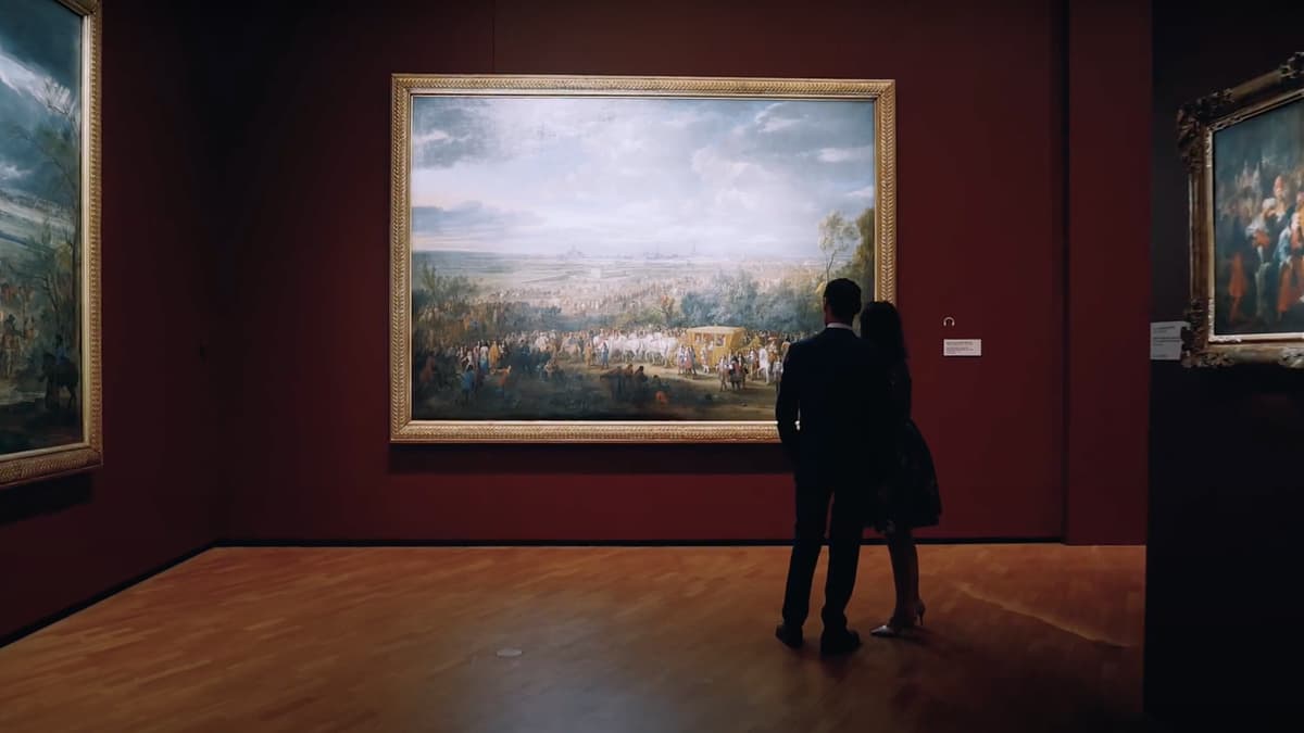 A video still of two people looking at an artwork in a gallery space