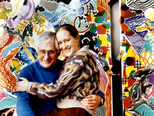 A couple embrace in front of a colourful artwork