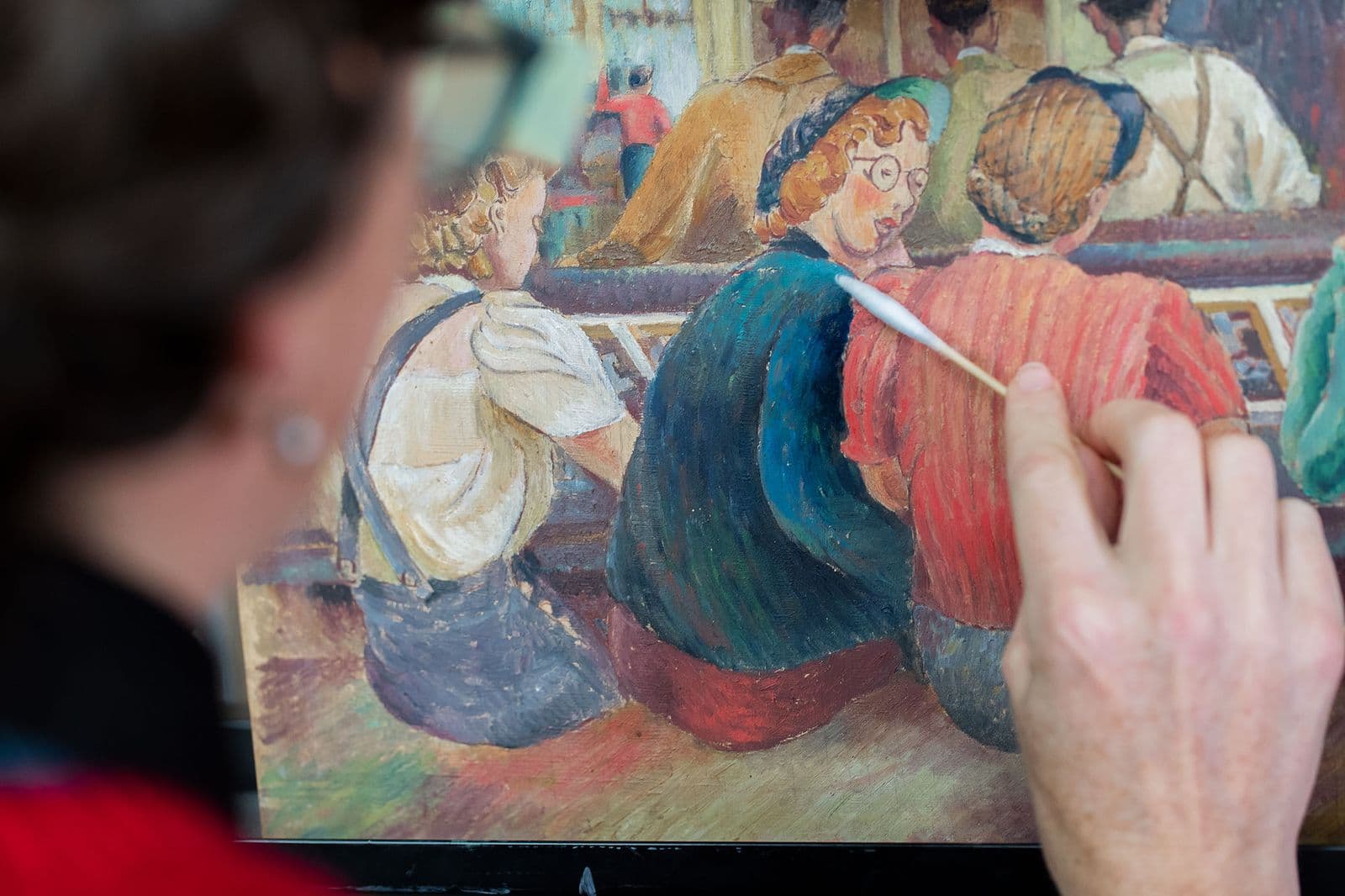 A woman uses a cotton bud to clean a painting