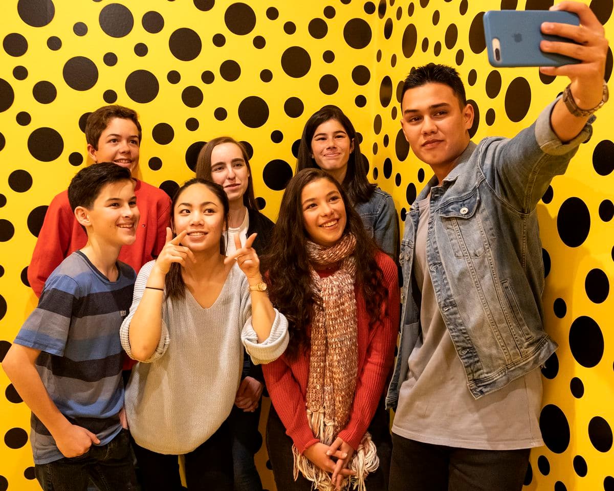 A group of people taking a selfie against a yellow backdrop with black spots