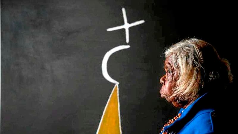 Photograph of Artist Mabel Juli looking side on with work of art behind her with black background, symbols and yellow shape.