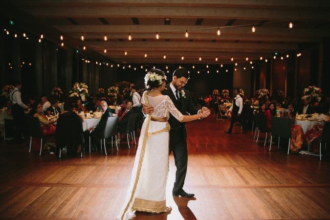 A bride and groom dance in a large room in front of a crowd