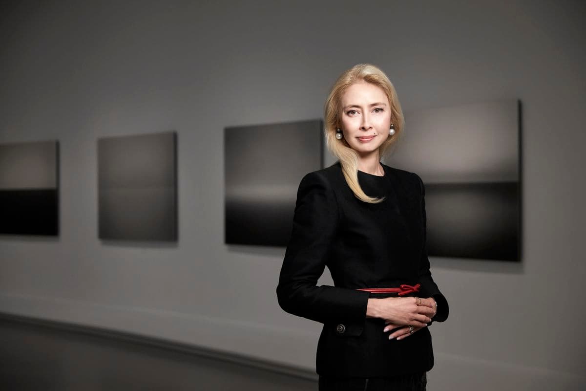 Blonde woman landscape portrait standing in an art gallery, white walls, paintings in the background
