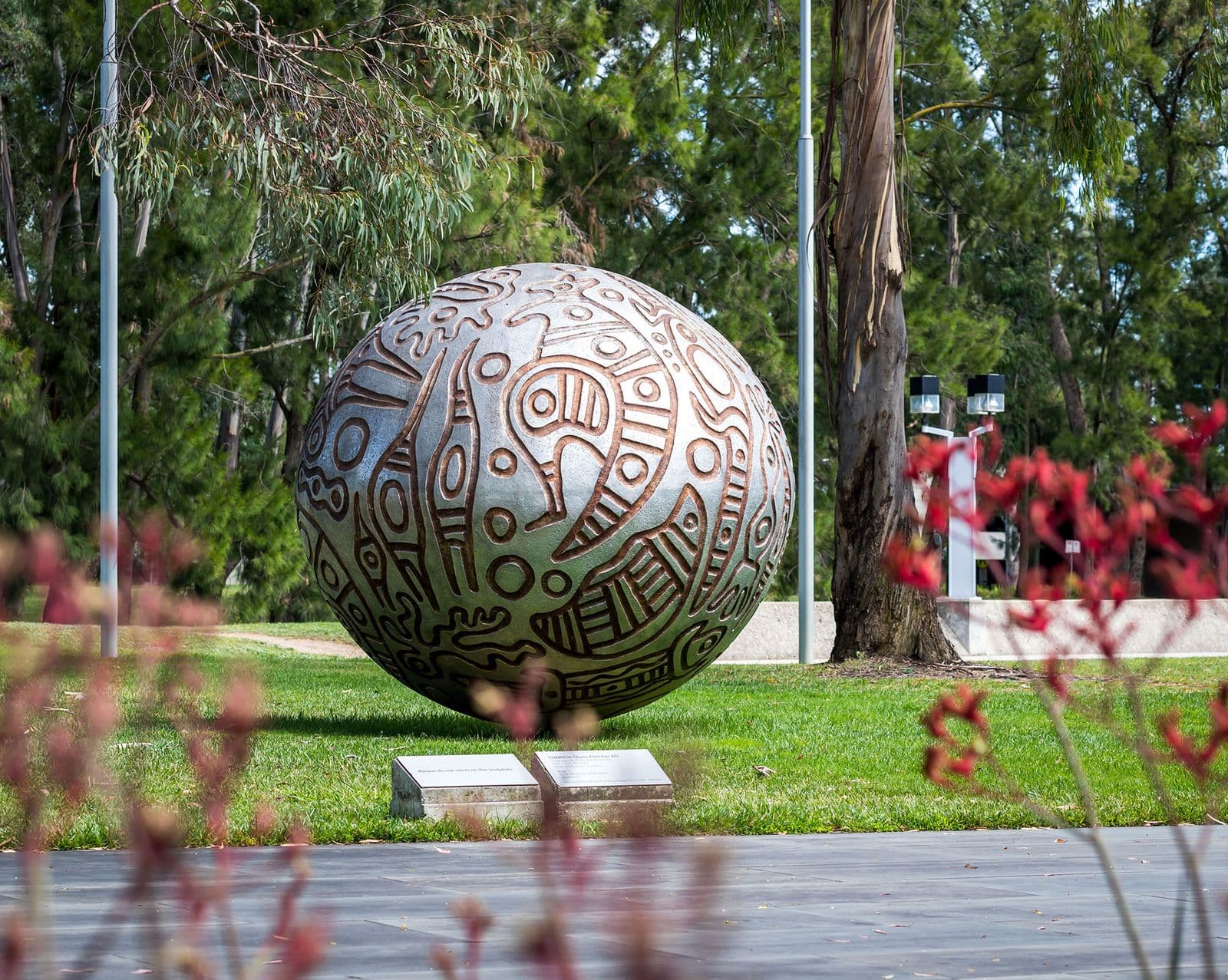 a large spherical metal sculpture with engraved markings sitting within a garden