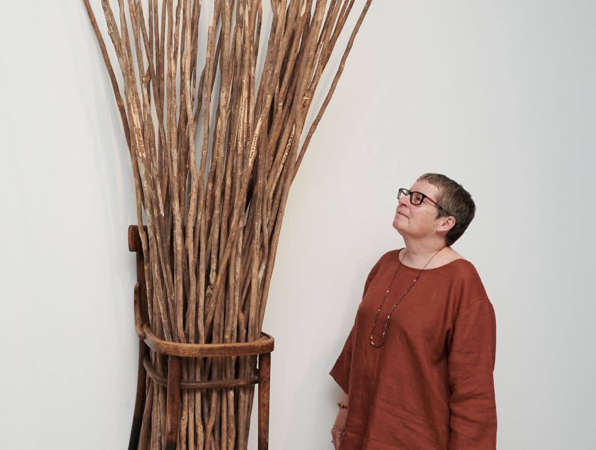 Image of artist Julie Gough standing with her work comprised of a bunch of wooden spears