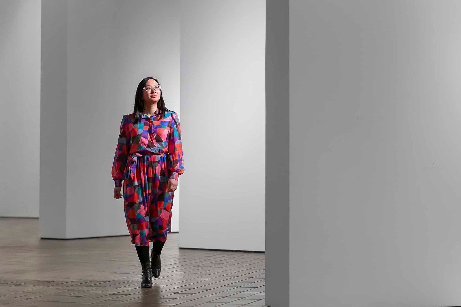 A woman in a colourful dress walks through an empty gallery.