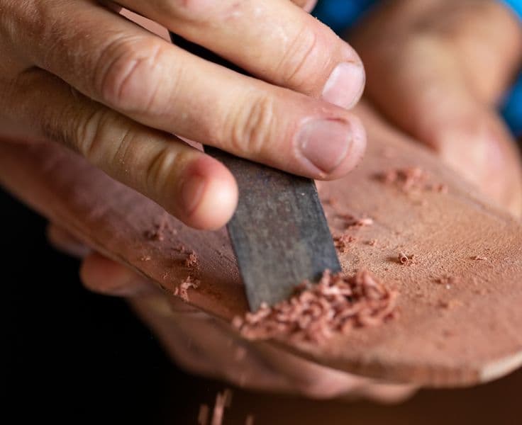 Close up photograph of artist carving with wood shavings