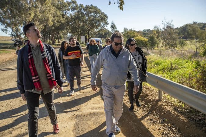 a group of people are walking along a path in the bush, heading towards the camera