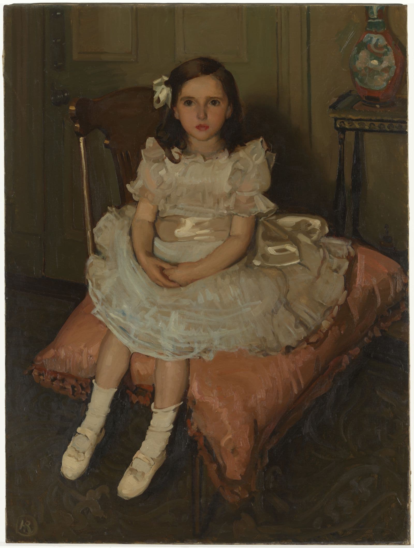 Portrait of a small child in a white frilly dress seated on a chair cushion