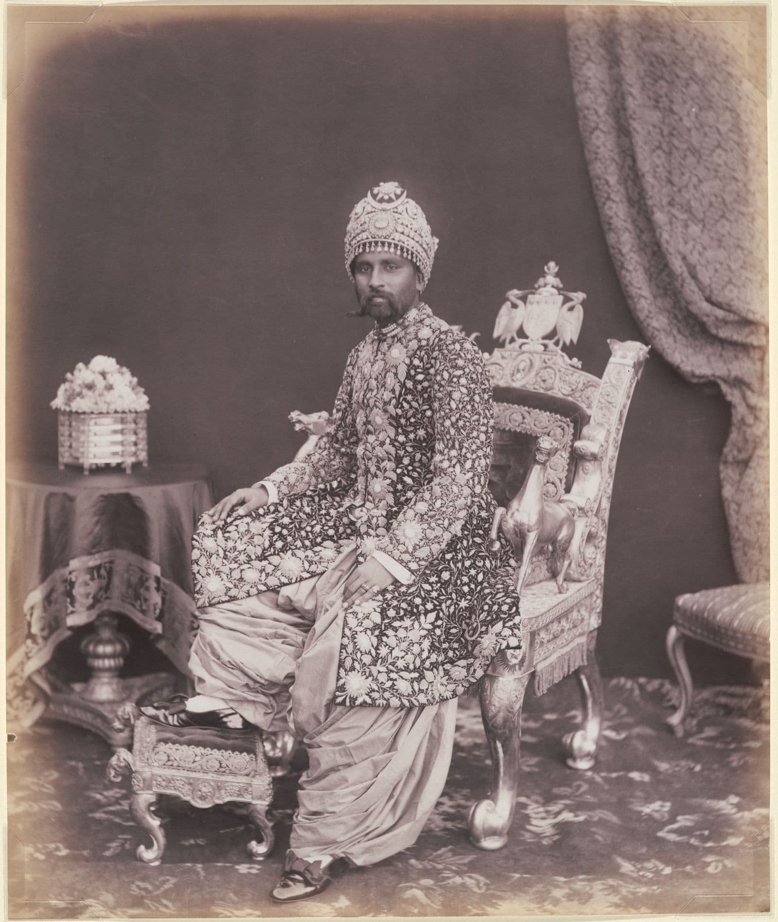 Black and white photograph of seated man in ornate clothing and crown