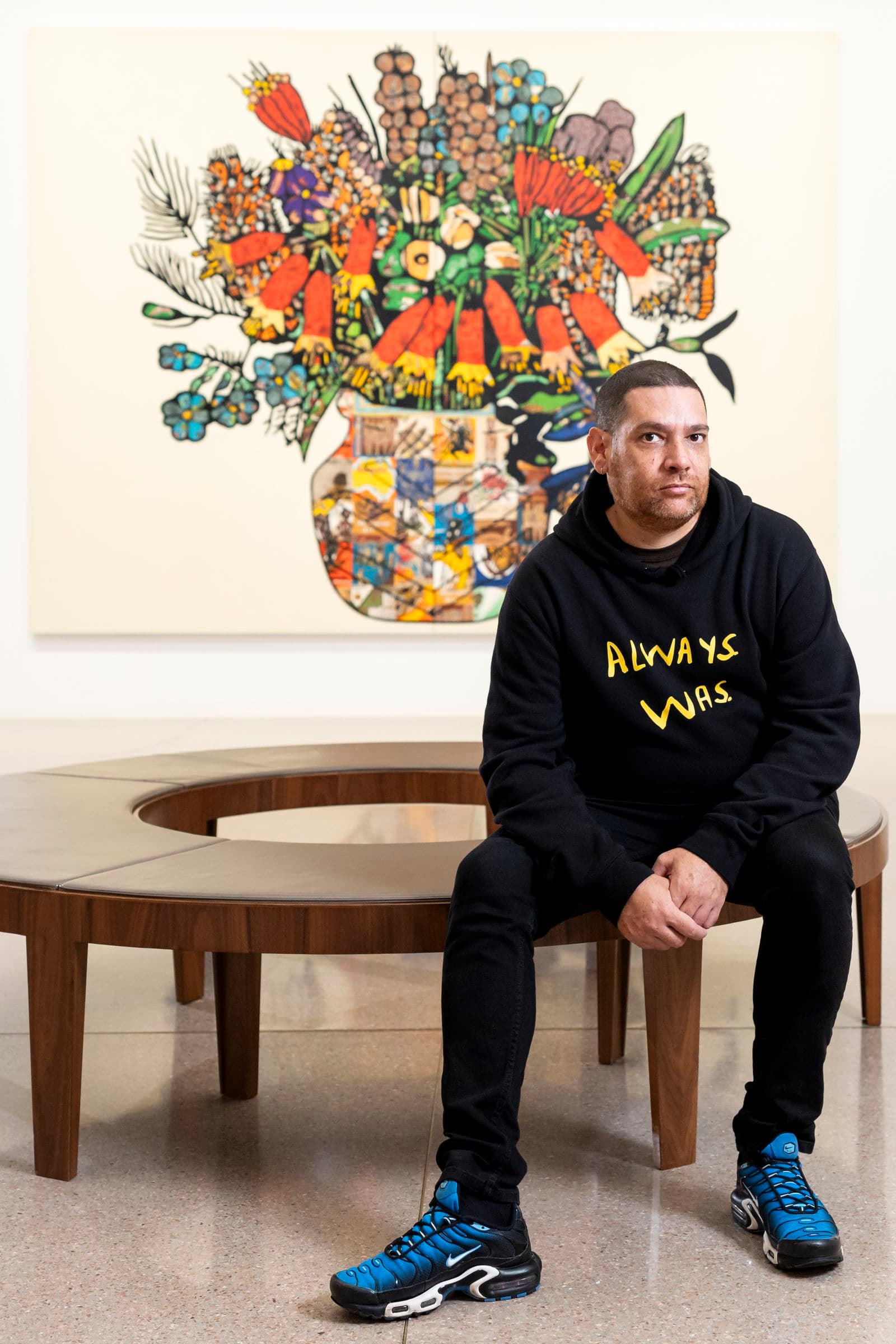 Photo of Tony Albert seated in front of an artwork in the National Gallery.