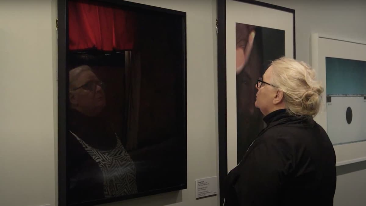 A video still of a woman looking at an artwork in a gallery space