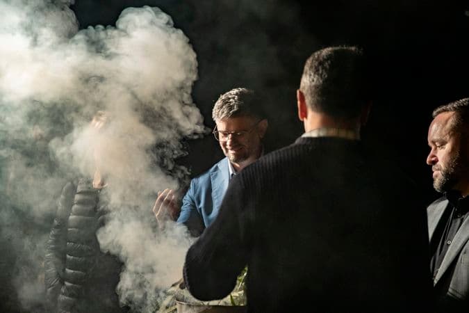 One man is holding a metal bucket that is emitting plumes of smoke from native leaves. Three other people are gathered around taking part in the smoking ceremony.
