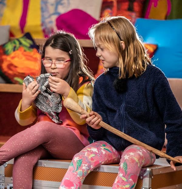 Two young girls are sitting on top of a large orange case, holding and examining objects