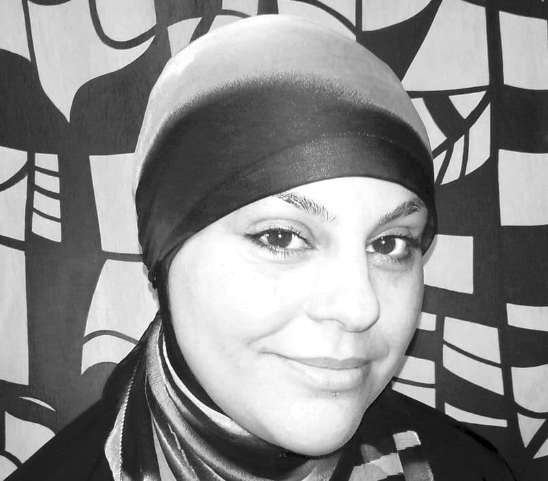 Portrait headshot of a female wearing a head scarf, in front of a patterned background