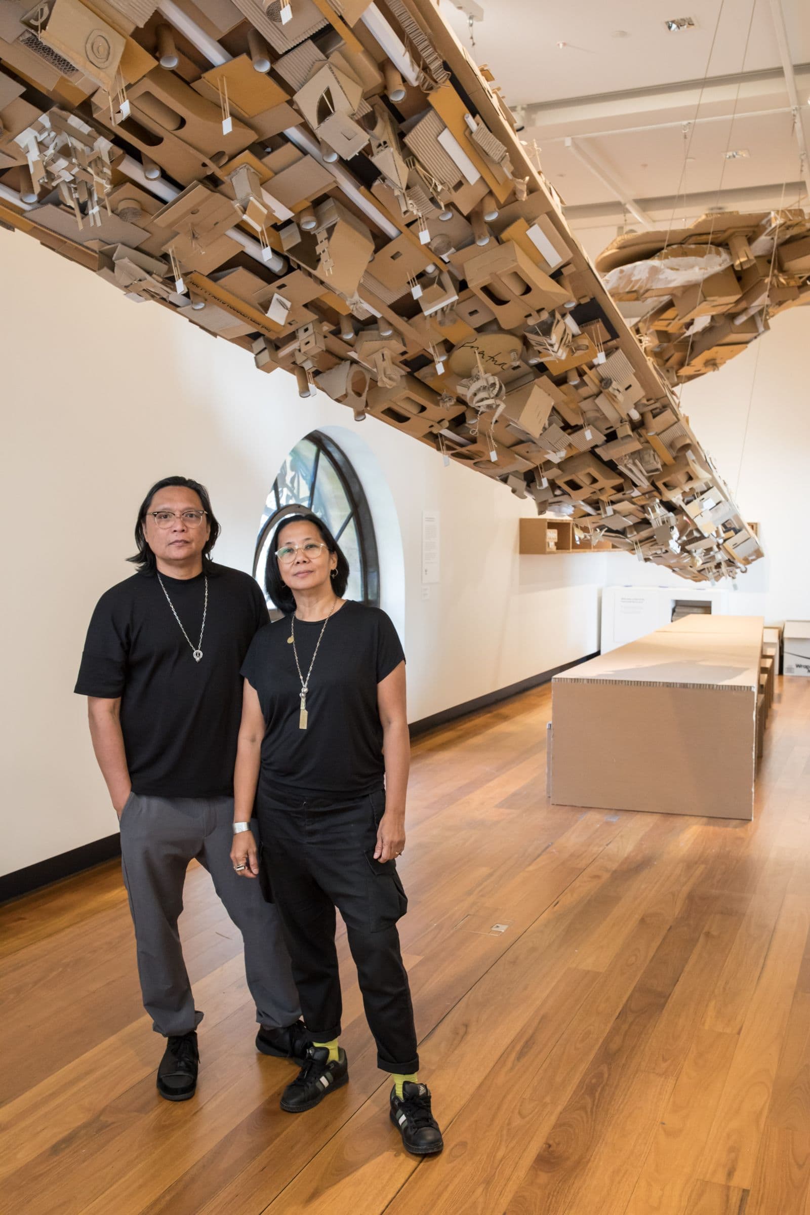 A portrait photo of two Philippine/Australian artists standing in front of their sculpture.