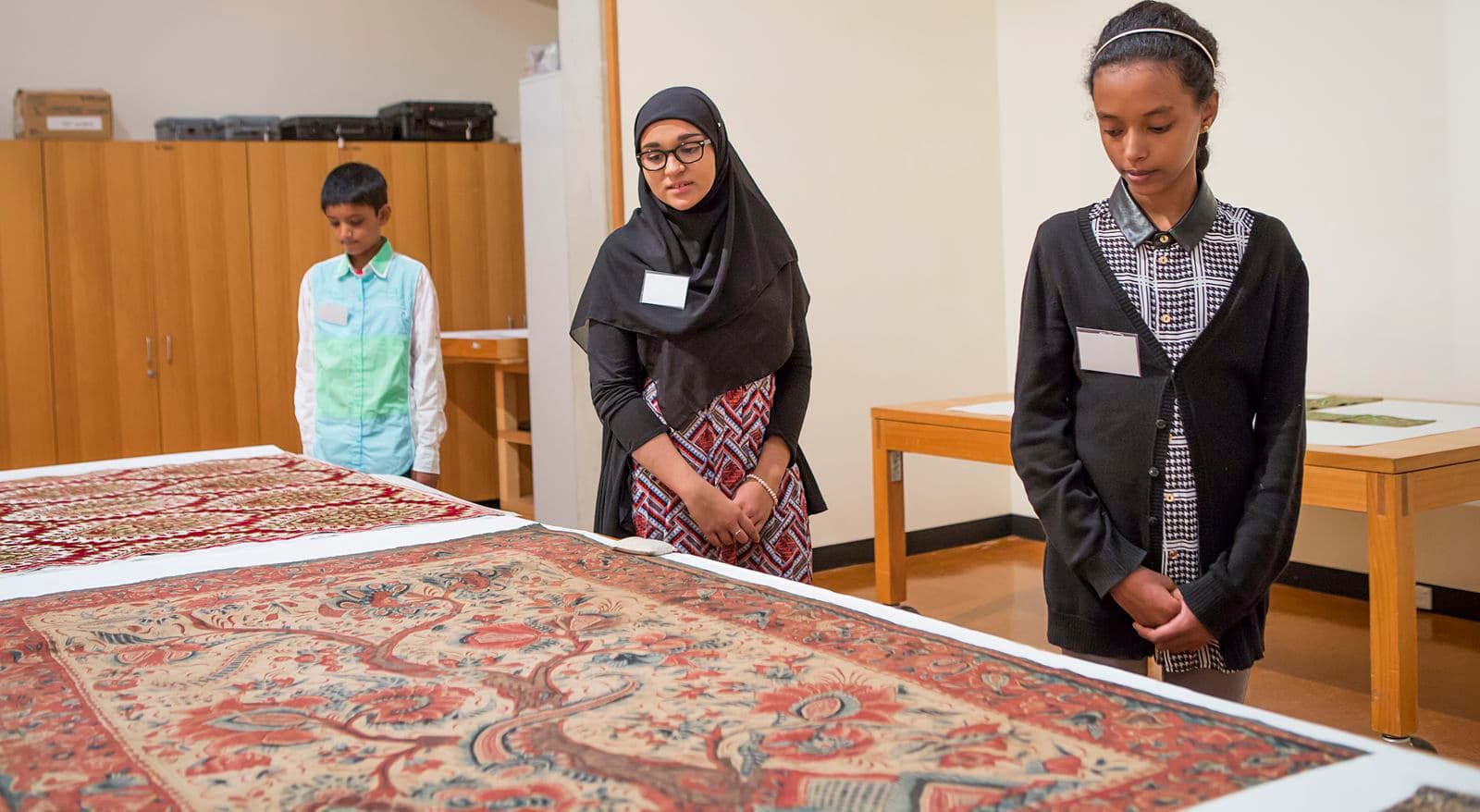 Three students looking at two textile works of art in the Gallery’s Collection study room