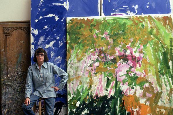 Joan Mitchell sits on a stool in front of two large painted canvasses
