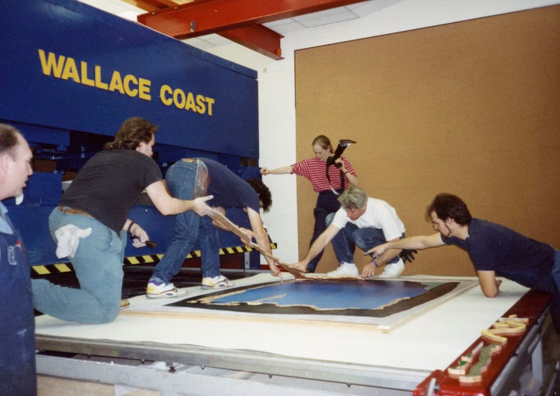 A team of people surround an artwork on the floor with a sign to the left saying "Wallace Coast"
