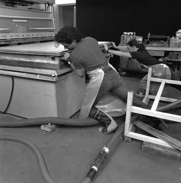Black and white photo of two men pushing the platen press