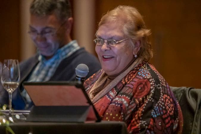 A close-up photo of a woman smiling as she give a speech from behind a lectern