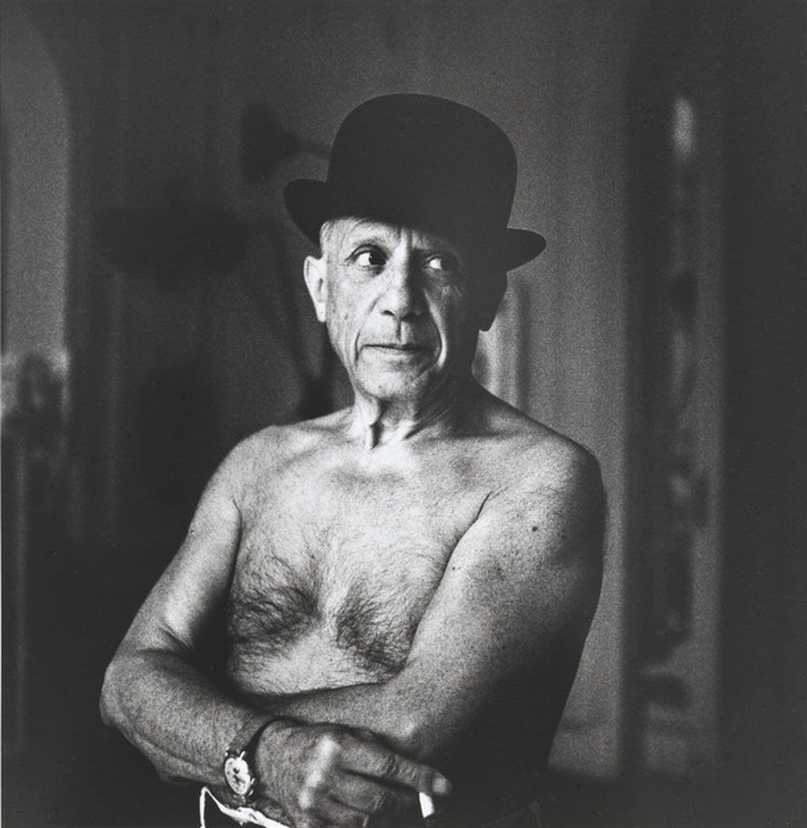 A photograph of a shirtless Picasso in a bowler hat smoking a cigarette.