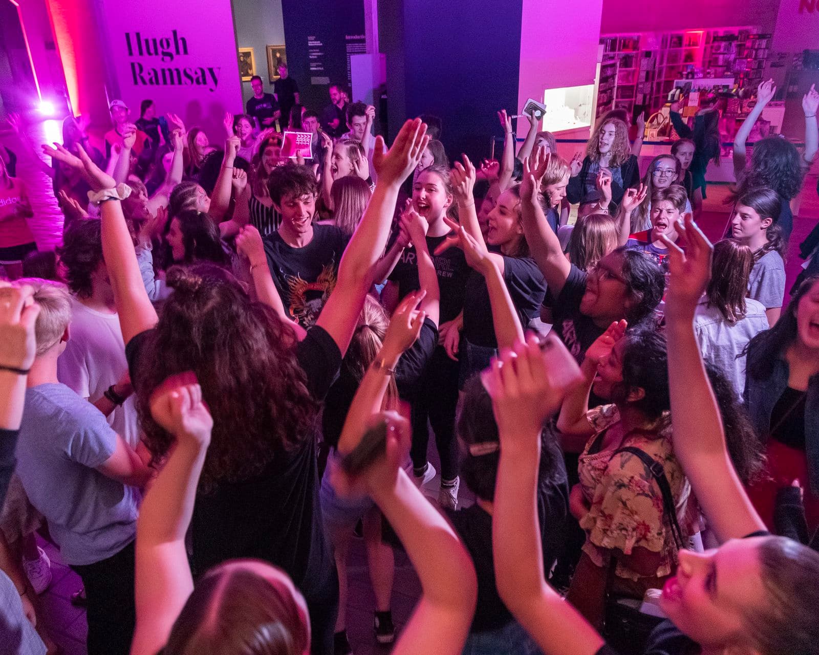 a group of young people are dancing with their arms up in the air under coloured purple lighting