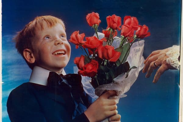 Picture of a young redheaded offering a bouquet of red roses to an unknown figure whose elderly hands are shown in the frame.