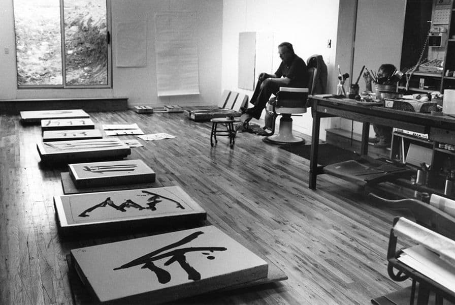 Black and white photograph of Robert Motherwell studying his newly drawn lithography stones for his 'Rites of passage' series in the barber's chair