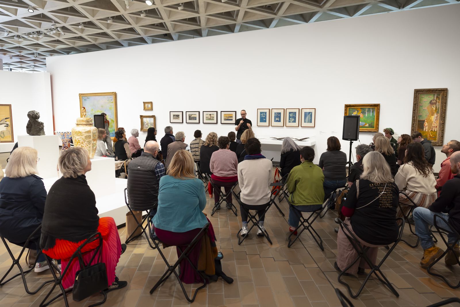 Photo of a group of people sitting in a gallery listening to someone talk