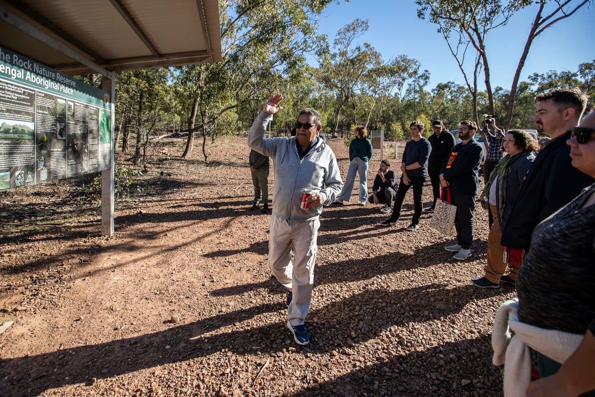 Outside a man in a grey tracksuit is talking to a group of people gathered around him
